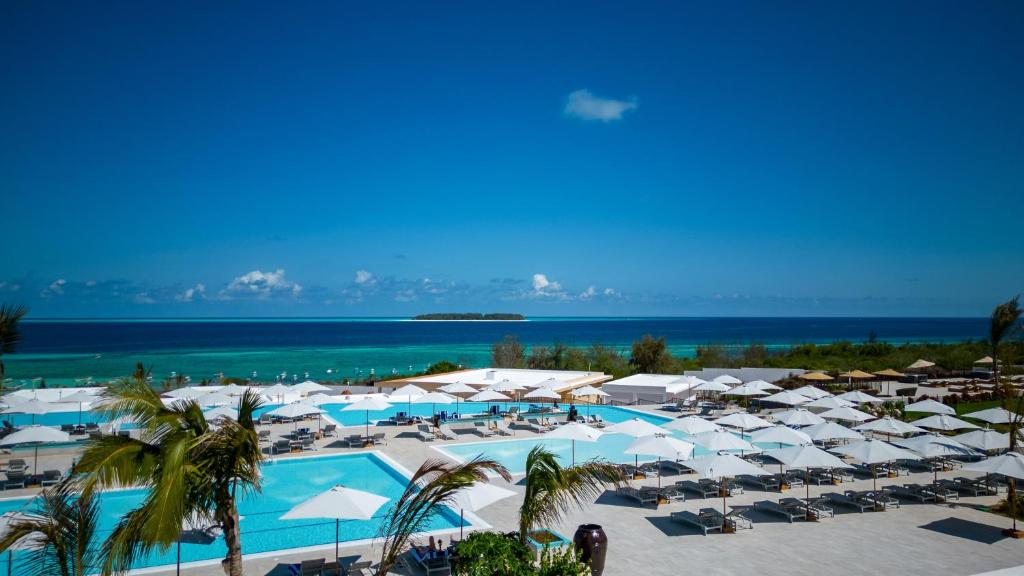 a large pool with white umbrellas and the ocean at The Mora Zanzibar in Matemwe