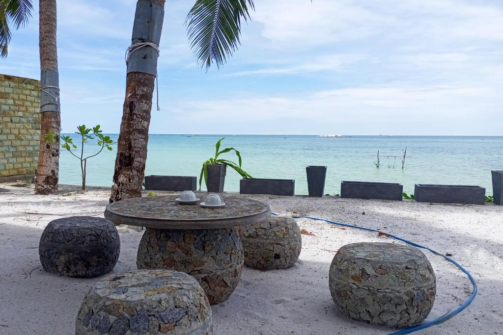 Watuduya Resort by The Lavana في Pasarbaru: طاولة وكراسي على شاطئ مع المحيط