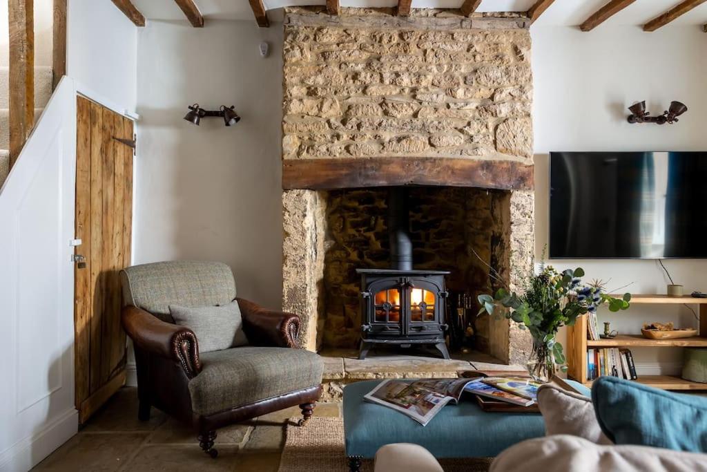 a living room with a stone fireplace and a chair at Charming 17th Century Cotswold Cottage in Adlestrop