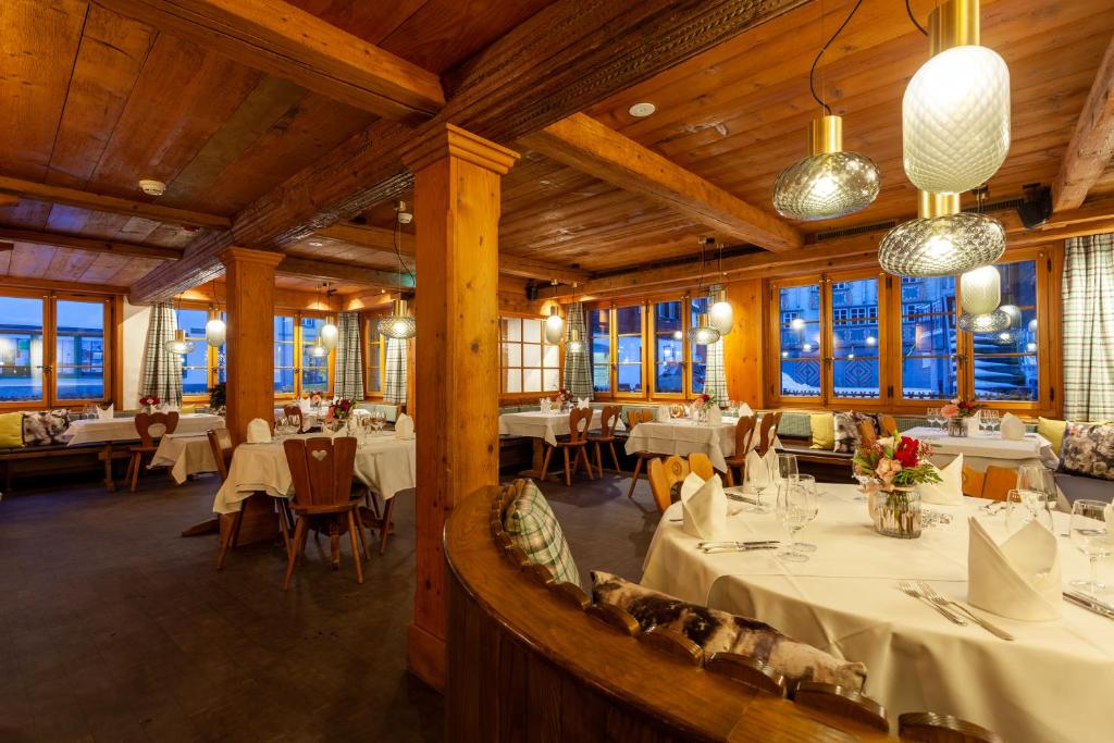 a restaurant with white tables and chairs and windows at Sonne Andermatt Swiss Quality Hotel in Andermatt