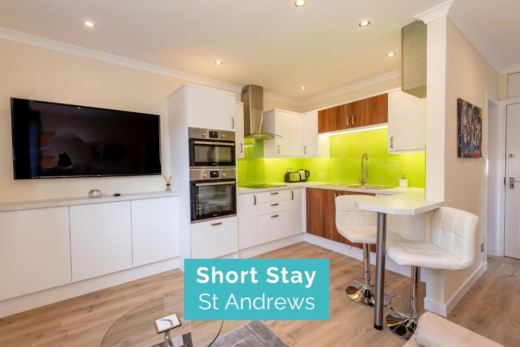 a kitchen with white cabinets and a flat screen tv at Pilmour Place - 30 Seconds to the Old Course! in St Andrews