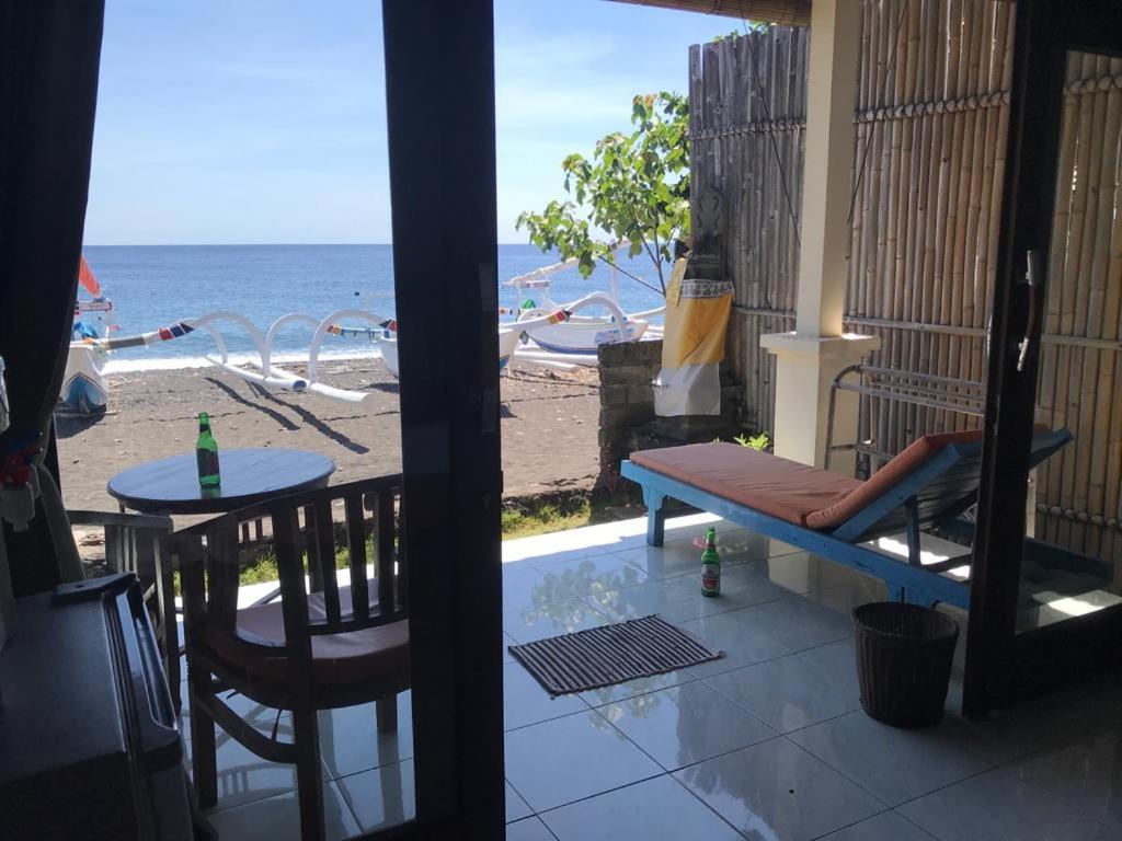 uma varanda com uma mesa e um banco e a praia em Tambun Sari Beach Homestay em Amed
