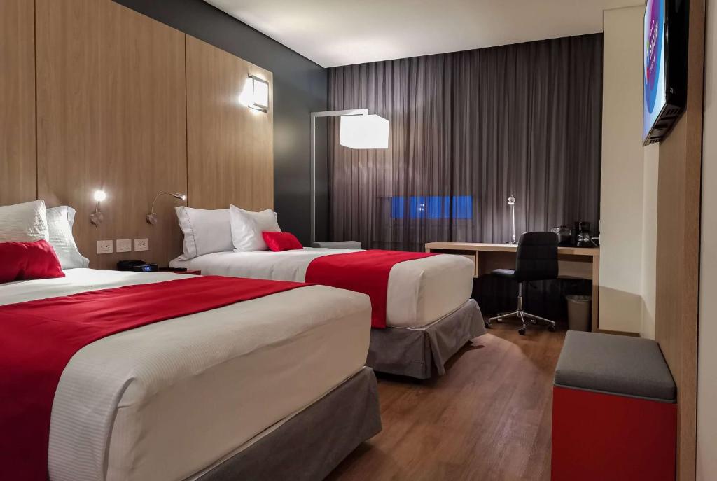 a hotel room with two beds and a desk at Ramada Encore by Wyndham Guadalajara Aeropuerto in Guadalajara