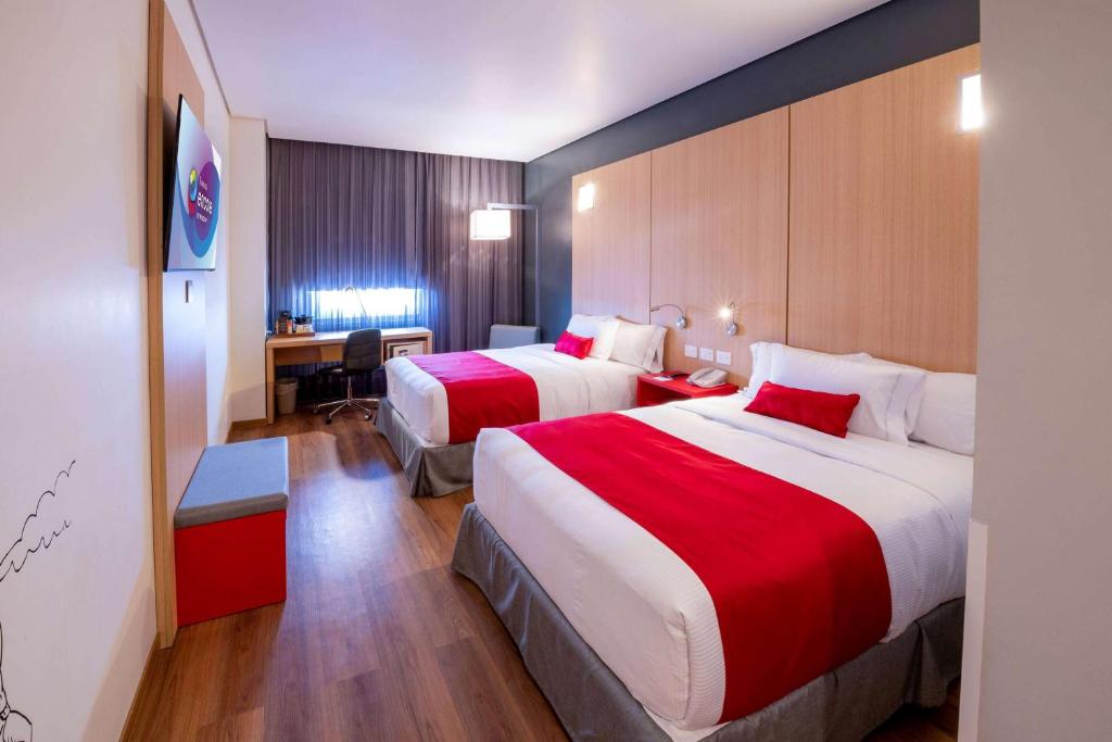 a hotel room with two beds and a desk at Ramada Encore by Wyndham Guadalajara Aeropuerto in Guadalajara