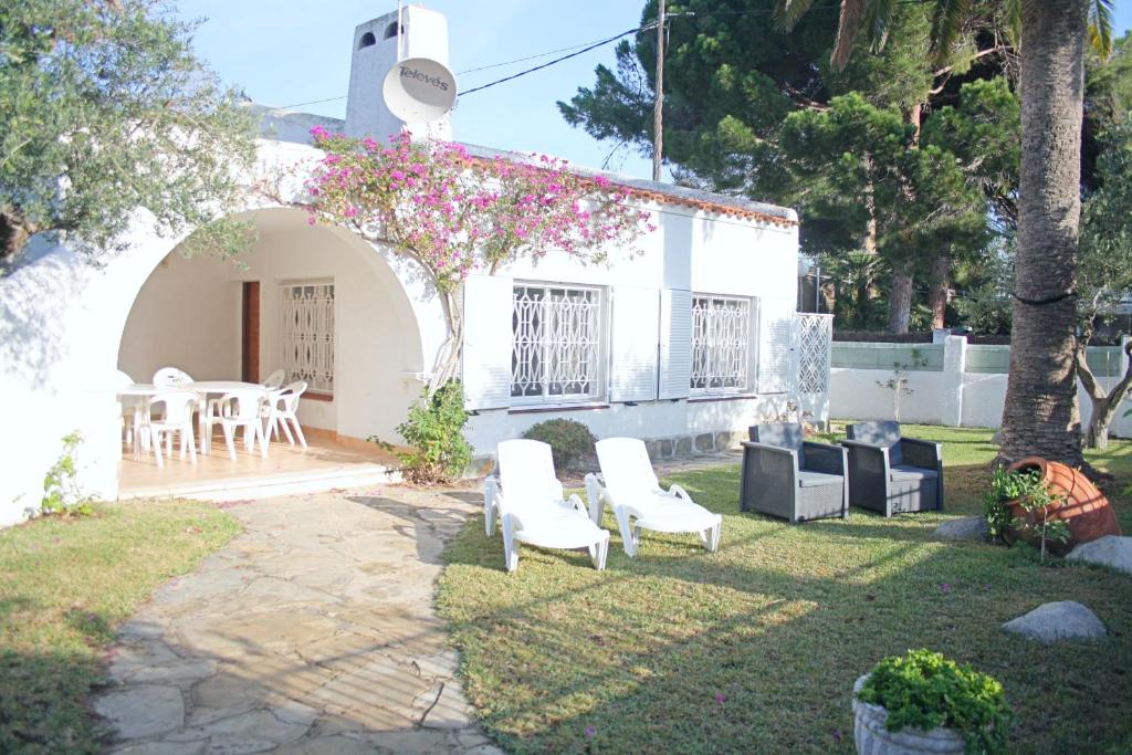 un patio con sillas blancas y una mesa con flores rosas en Charming seafront villa, en Cambrils