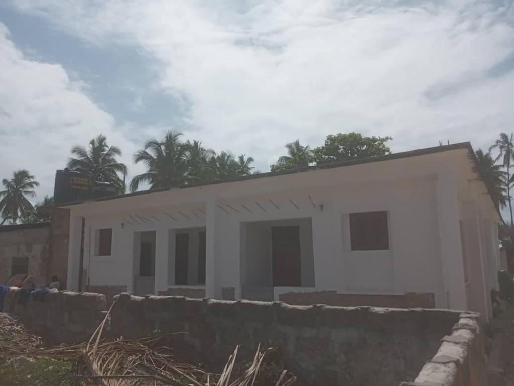 une maison blanche avec un mur en pierre devant elle dans l'établissement Iddi House, à Jambiani