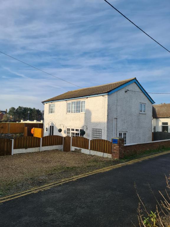 a white house with a fence on the side of a road at Resthaven Cottage in Mablethorpe