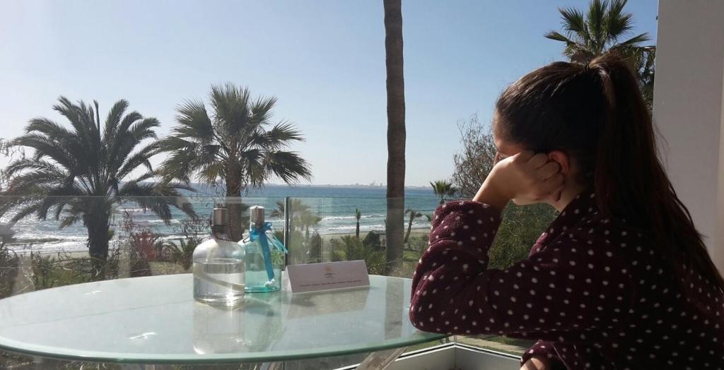 uma mulher sentada numa mesa a olhar para o oceano em Sandy Beach Apartment 13 em Voroklini
