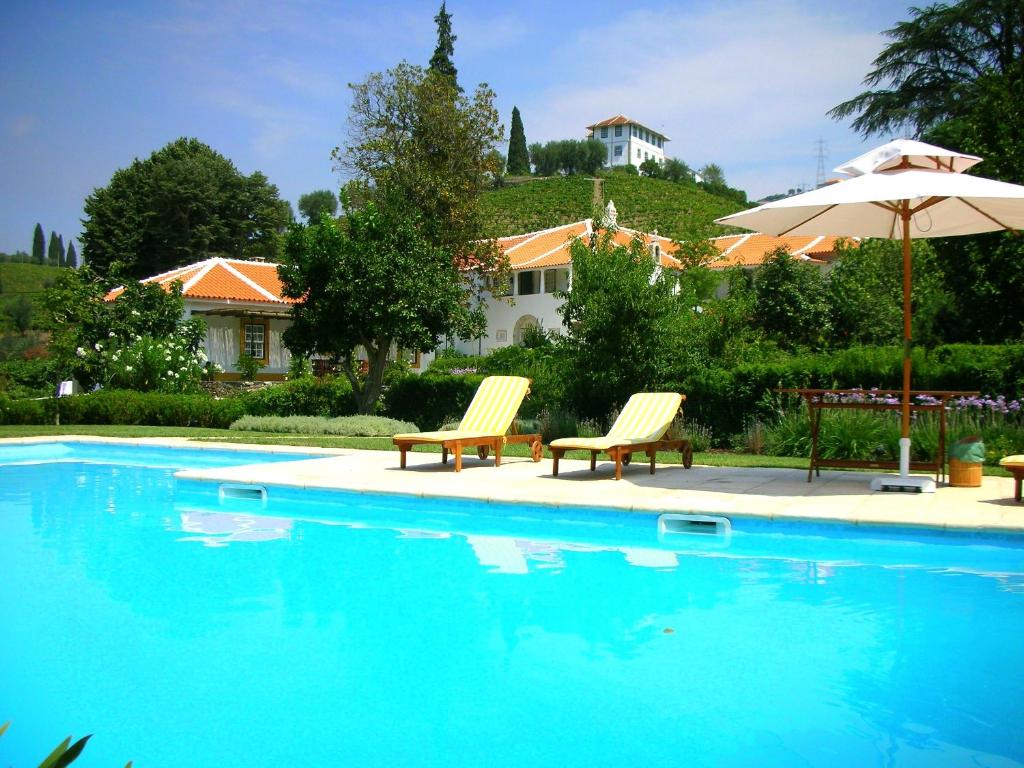 a swimming pool with two chairs and an umbrella at Casa da Azenha in Peso da Régua