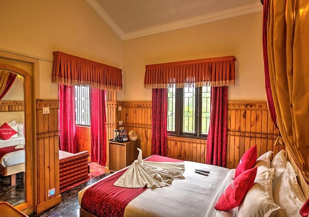 a bedroom with a large bed with red curtains at Pine Borough Inn in Kodaikānāl