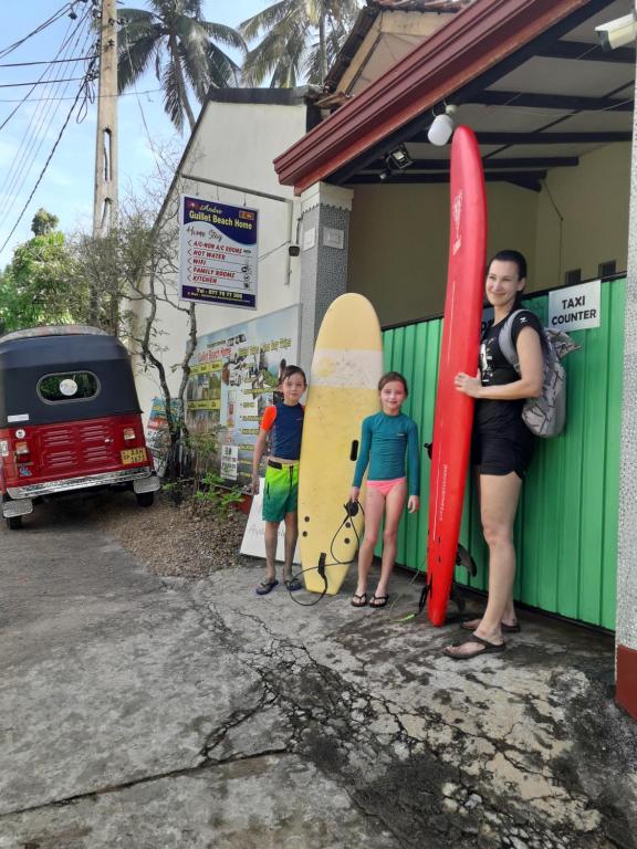een vrouw en twee kinderen die naast surfplanken staan bij Guillet Beach Home in Matara