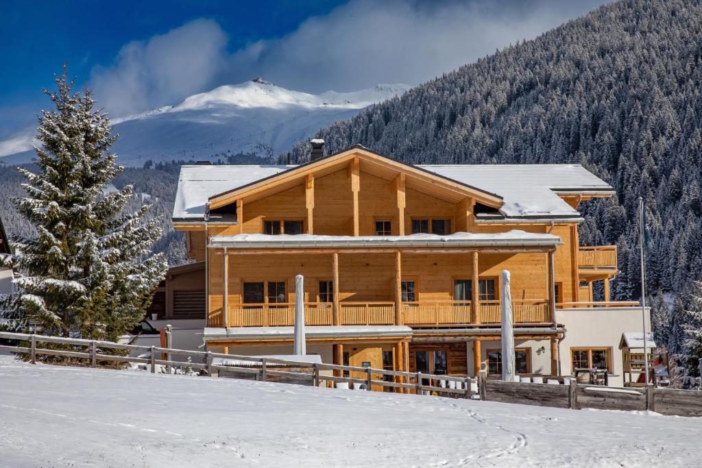 a log house in the snow with a snow covered mountain at Boutique Hotel Schraemli's Lengmatta in Davos