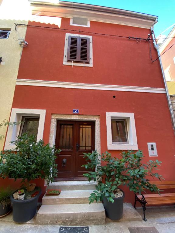 a red building with a door and some plants at Guesthouse Riba in Vrsar