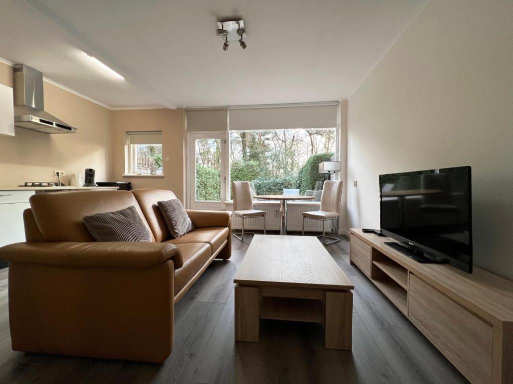 ein Wohnzimmer mit einem Sofa und einem Flachbild-TV in der Unterkunft Bosvakantie Veluwe - Huisje 54, Hoefbos, Otterlo in Otterlo