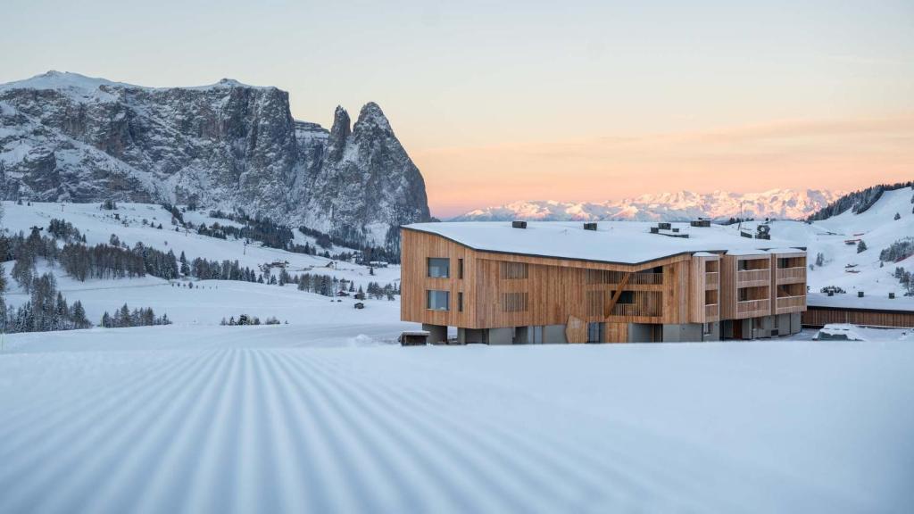 a building in the snow with a mountain in the background at ICARO Hotel in Alpe di Siusi