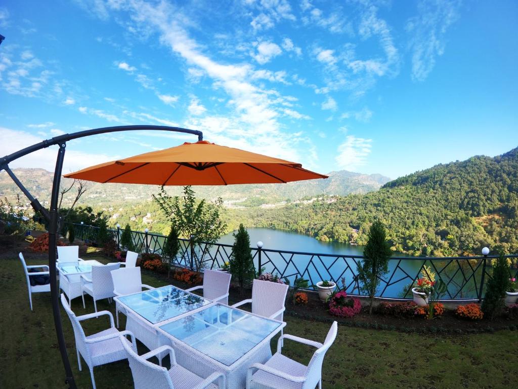 une table et des chaises avec un parasol et un lac dans l'établissement The Lake Ambience Resort, à Bhimtal