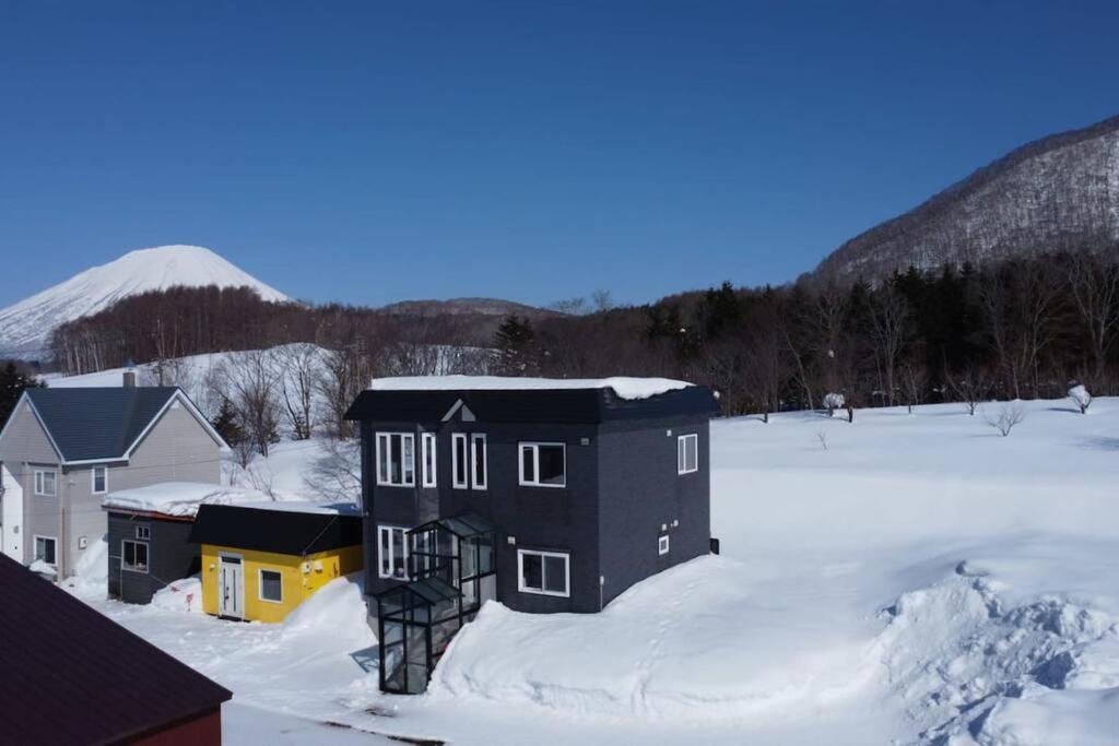 ein schwarzes Gebäude im Schnee mit einem Berg im Hintergrund in der Unterkunft Rusutsu Kuma House in Rusutsu