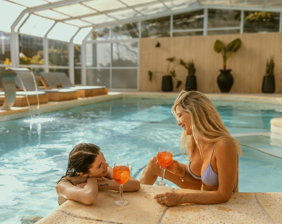 un hombre y una mujer sentados en una piscina con bebidas en La Galeria - Hotel Boutique Cariló en Cariló