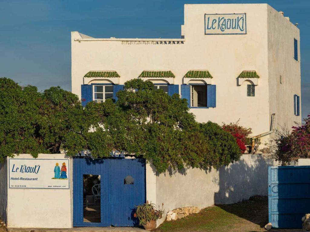 a building with a blue door and a tree at Hotel-Restaurant Le Kaouki in Sidi Kaouki
