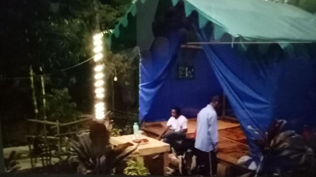 dos hombres sentados en una mesa en una tienda azul en Glamping Kalimarno Wonosalam, en Tukum