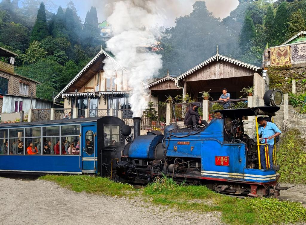 Ein blauer Zug fährt auf einer Strecke mit Leuten darauf. in der Unterkunft Marigold Manor Homestay in Darjeeling