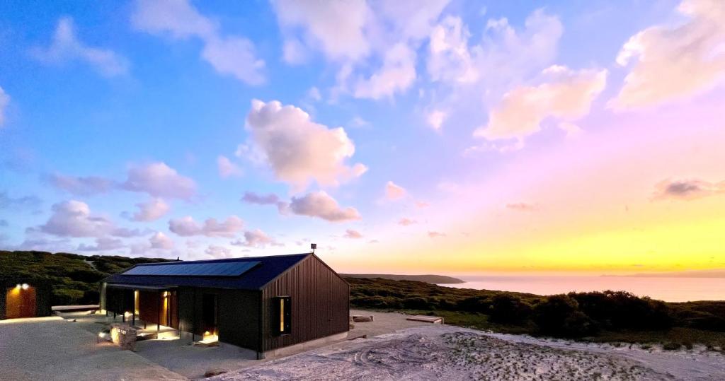 a house on the beach with a sunset in the background at Native Dog Cabin in Bremer Bay