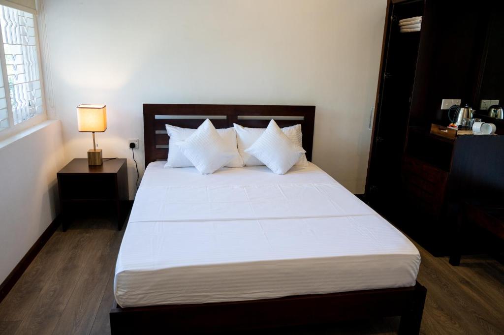 una camera da letto con un grande letto con lenzuola e cuscini bianchi di Avega Urban - Colombo 07 a Colombo