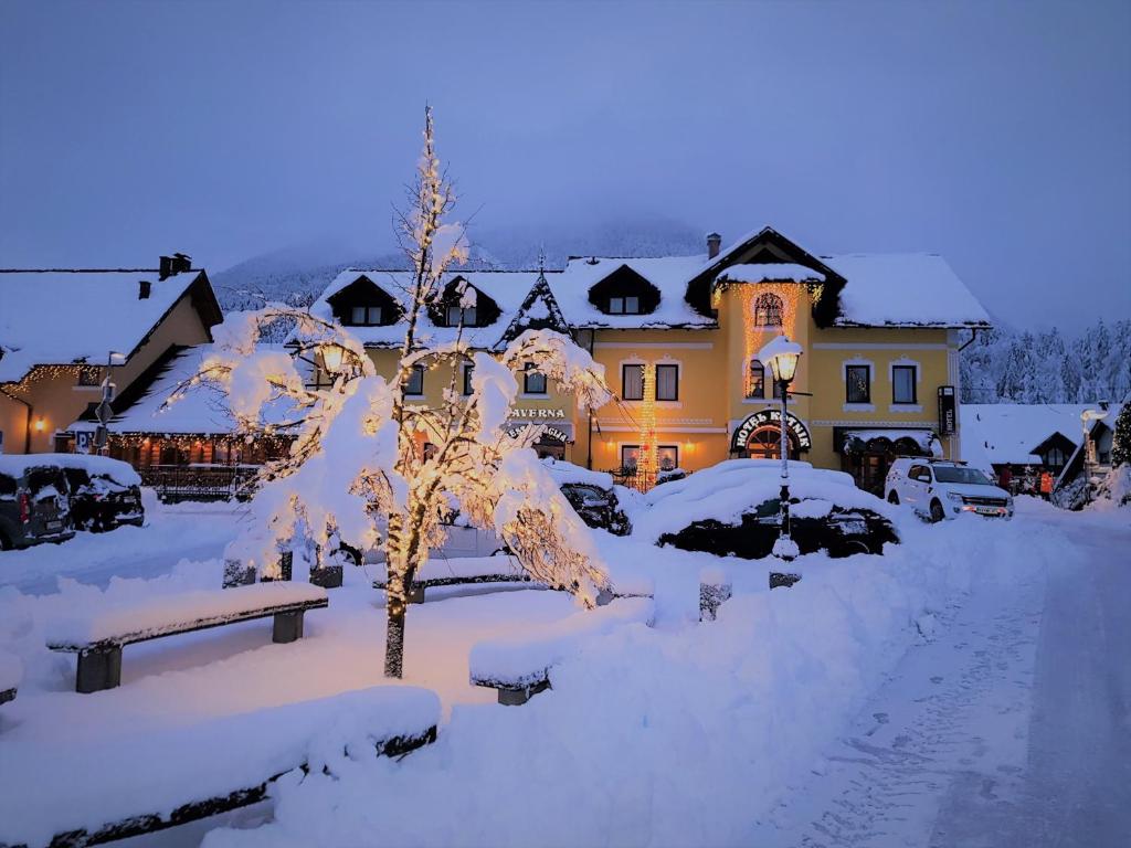 a house covered in snow with a tree in the yard at Hotel Kotnik in Kranjska Gora