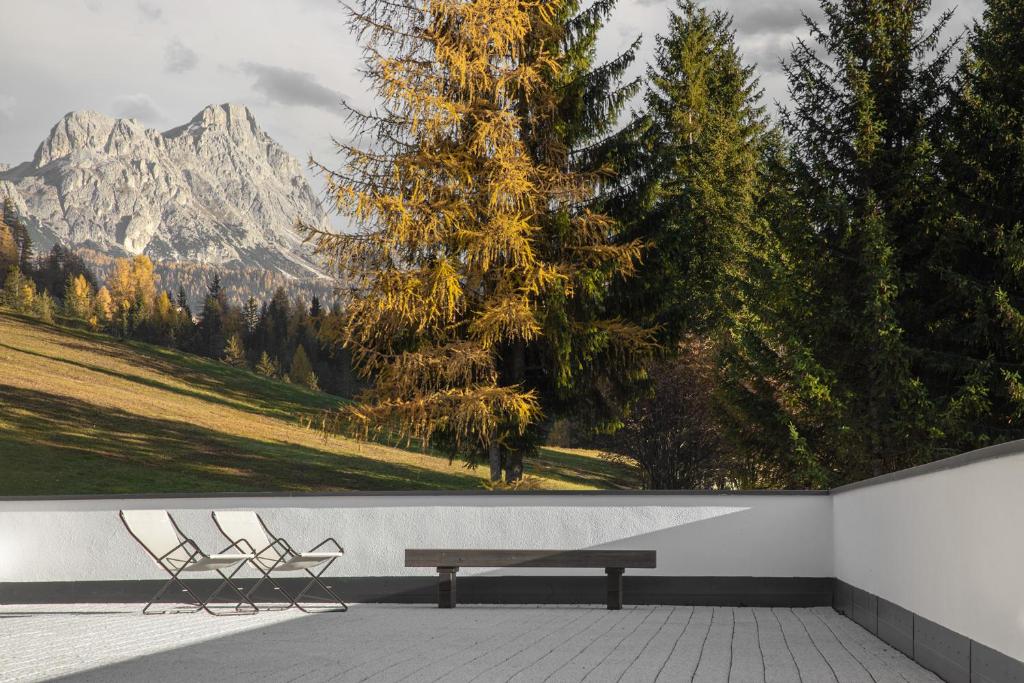 two chairs and a bench in front of a wall with mountains at Apartments Roda de Ciar in Badia