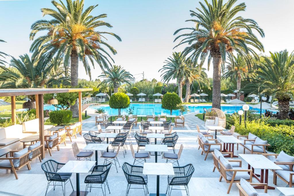 restauracja ze stołami, krzesłami i palmami w obiekcie May Beach Hotel w Retimnie