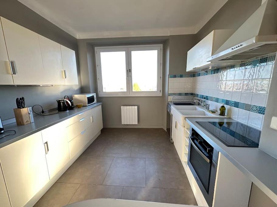 a kitchen with white cabinets and a large window at Appartement de charme - Lorient in Lorient