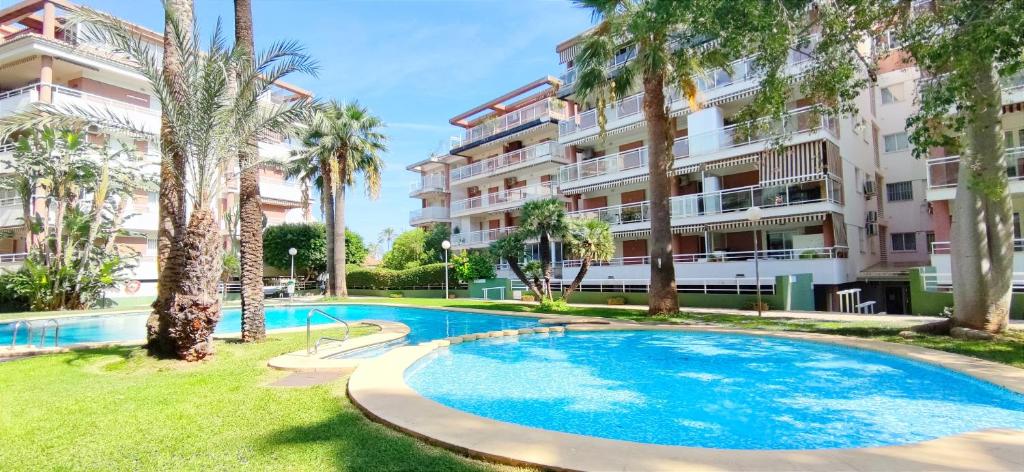 a swimming pool in front of a building with palm trees at Apartamento Dianium by DENIA COSTA in Denia