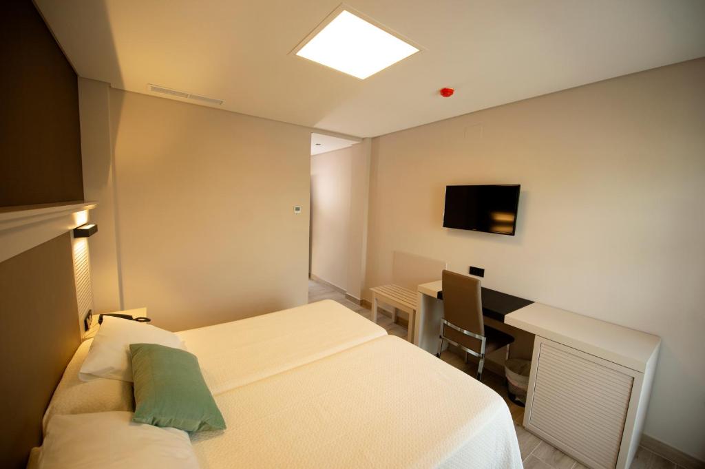 a room with two beds and a desk and a television at Hotel Diufain in Conil de la Frontera