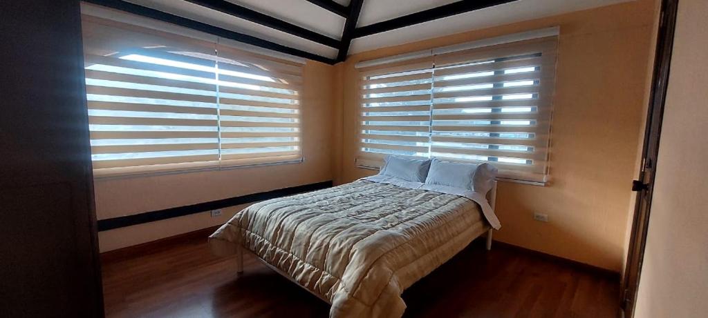 a bedroom with a bed and two windows with blinds at Hospedaje in Quito