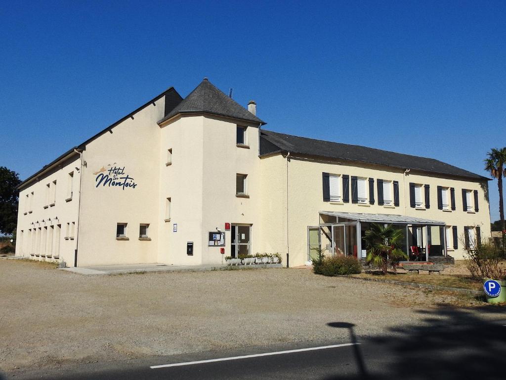 un grand bâtiment blanc avec un toit noir dans l'établissement Hotel Les Montois, à Céaux