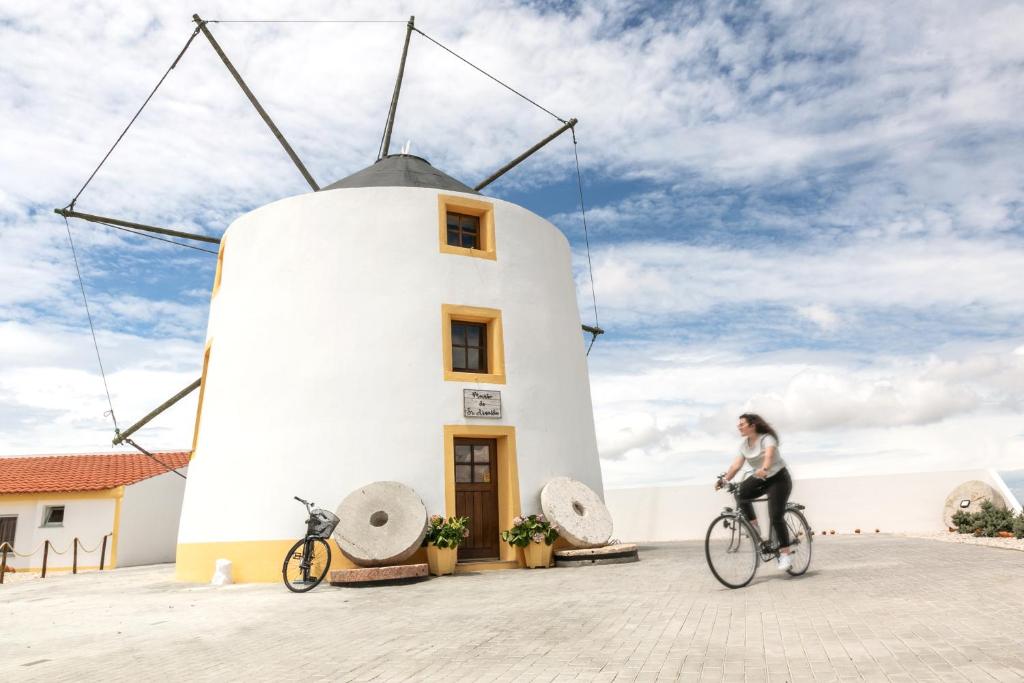 una mujer montando una bicicleta delante de un molino de viento en Moinho do Sr. Arnaldo, en Atouguia da Baleia
