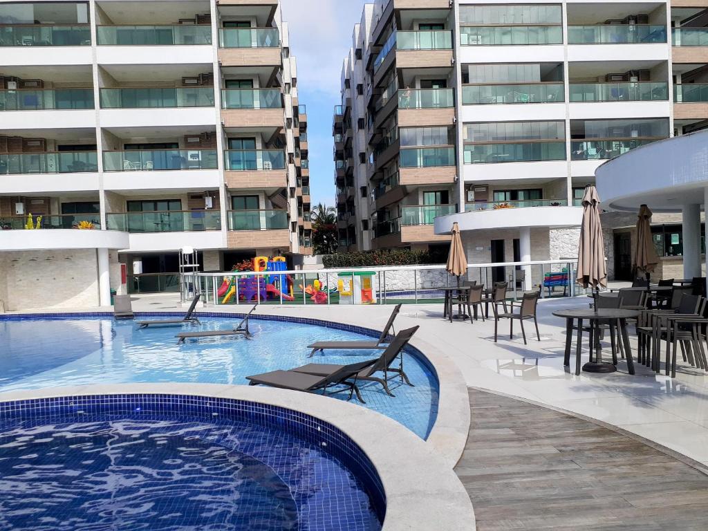 una piscina con mesas y sillas y un edificio en Frente mar 3 quartos Praia dos Anjos Residence, en Arraial do Cabo