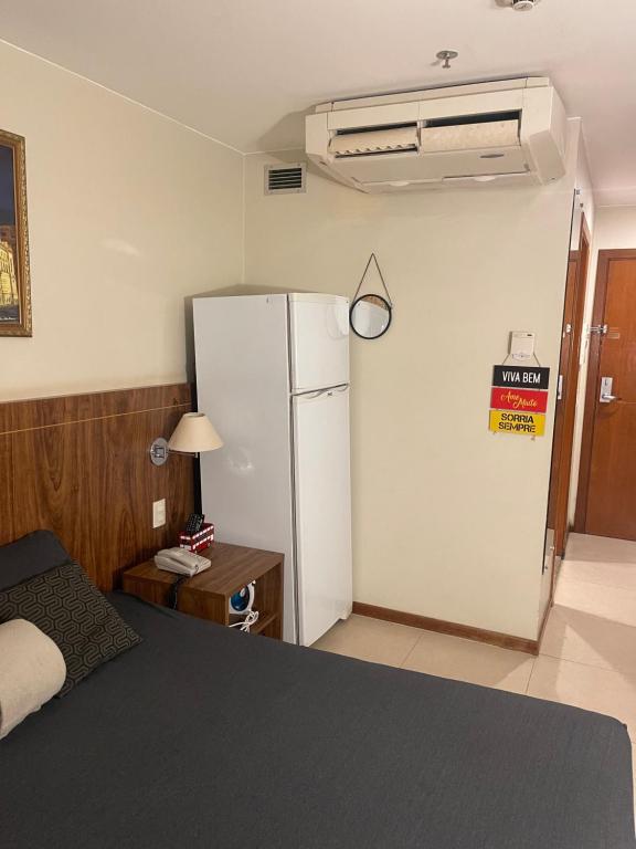 a room with a refrigerator and a table and a bed at PROMOÇÃO EXECUTIVA COM BANHEIRA E FLATS SEM BANHEIRA- Melhor Hotel De Taguatinga in Taguatinga