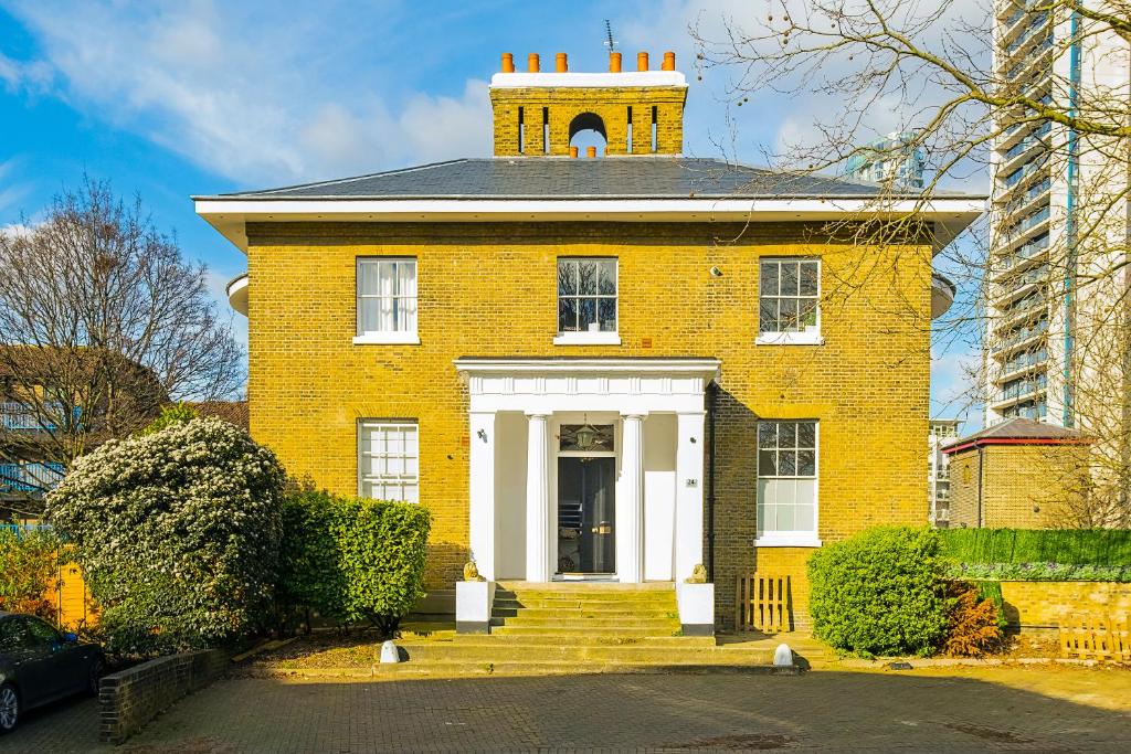 a yellow brick house with a tower on top of it at Larger Groups Canary Wharf Apartment with Large Garden & Parking in London