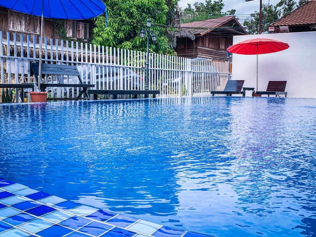 a swimming pool with a red umbrella and two benches at Bountang Mountain View Riverside Hotel in Vang Vieng