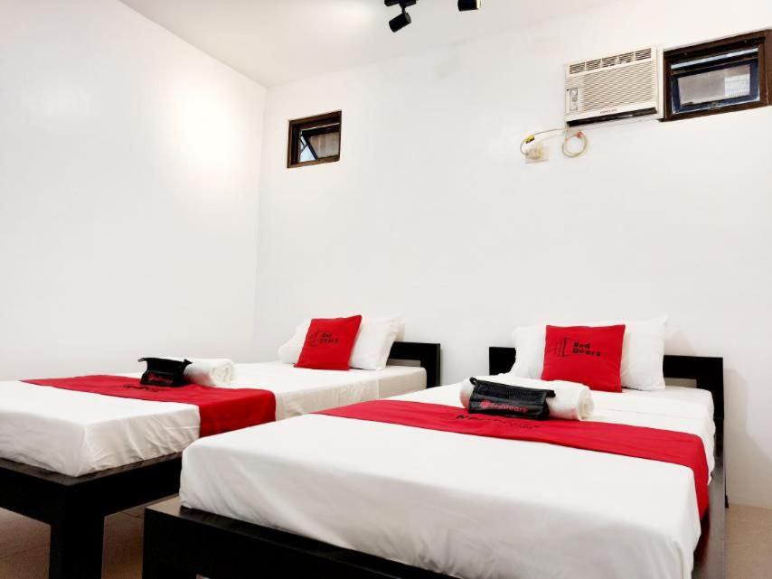 Duas camas num quarto com paredes brancas e almofadas vermelhas em RedDoorz @ San Antonio Binan em Biñan