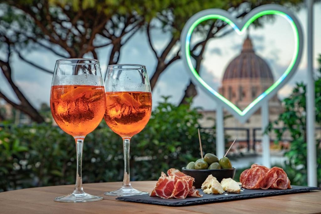 two glasses of wine and a plate of fruit on a table at Fragrance Hotel St. Peter in Rome