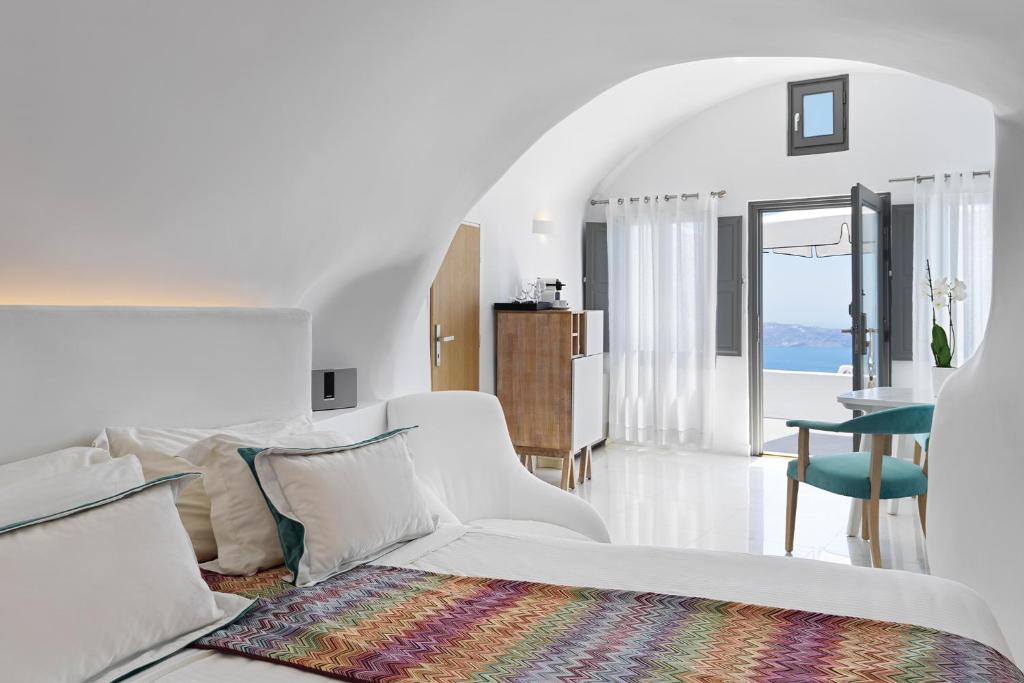 a white room with a white couch and a table at Katikies Chromata Santorini - The Leading Hotels of the World in Imerovigli