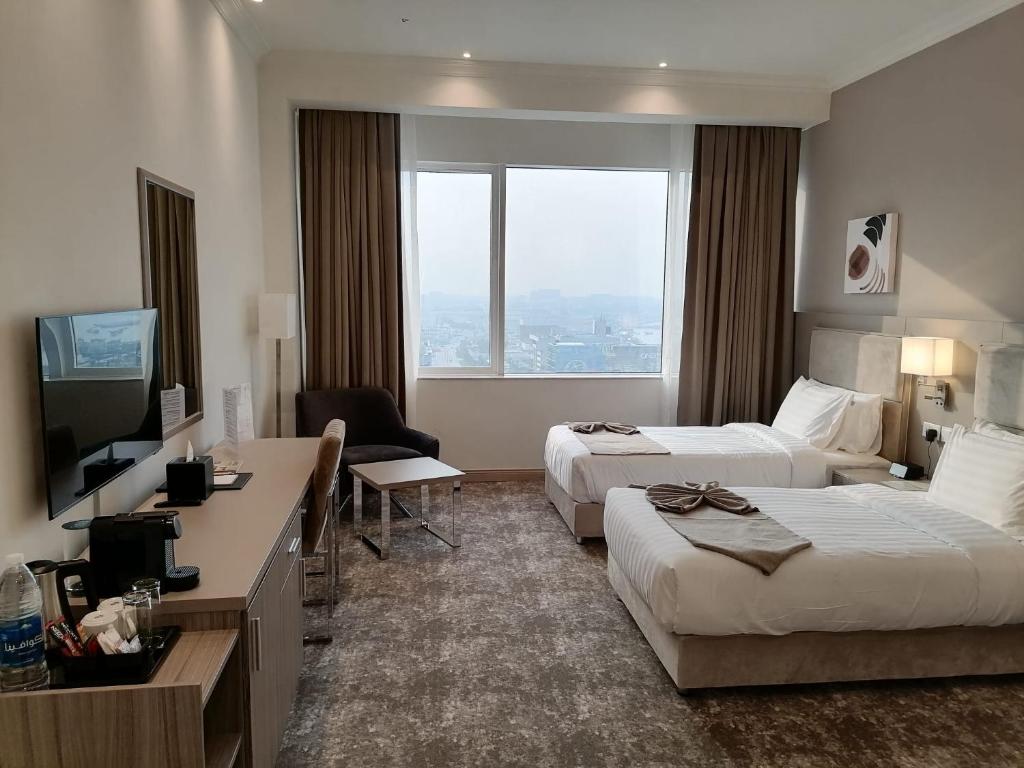 Gloria Hotel & Suites Doha في الدوحة: غرفه فندقيه سريرين وتلفزيون