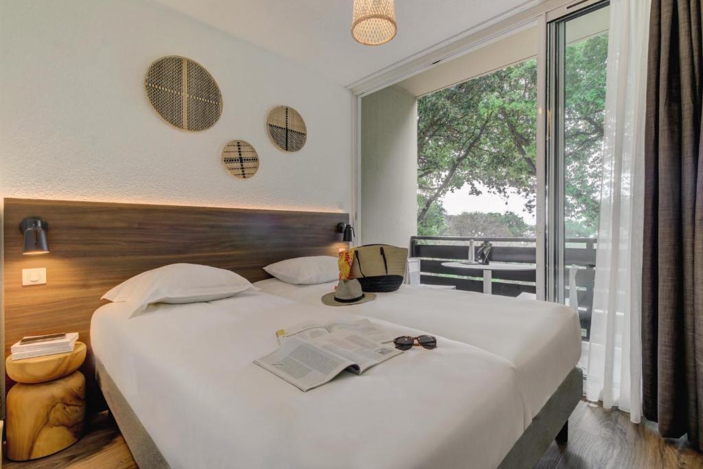 a bedroom with a bed with a book and a window at Belambra Clubs Presqu&#39;île De Giens - les Criques in Hyères