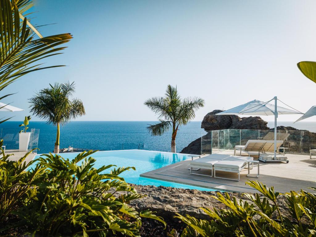 einen Pool mit Stühlen und das Meer im Hintergrund in der Unterkunft Grand Horizon Luxury Boutique Apartments in Puerto Rico de Gran Canaria