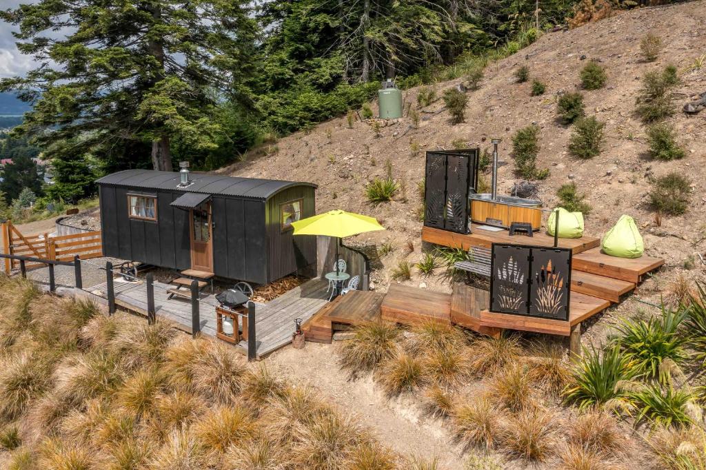 a black tiny house with a deck and a yellow umbrella at The Shepherds Hut - boutique retreat. in Hanmer Springs