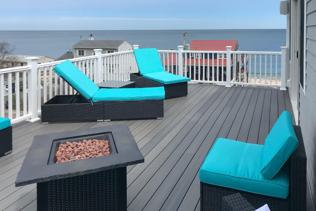 a deck with blue chairs and a fire pit and the ocean at Bayberry Beauty in Nameloc Heights