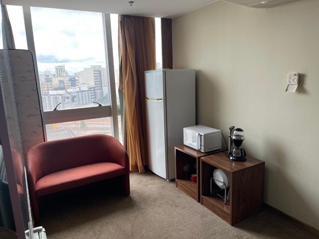 a room with a refrigerator and a chair and a window at PROMOÇÃO EXECUTIVA COM BANHEIRA E FLATS SEM BANHEIRA- Melhor Hotel De Taguatinga in Taguatinga