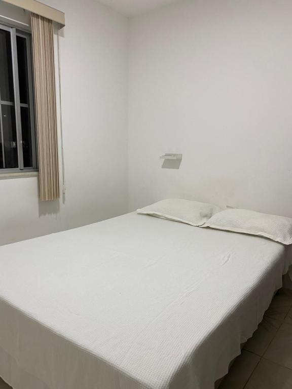 Cama blanca en habitación con ventana en Seu apartamento em Ilhéus, en Ilhéus